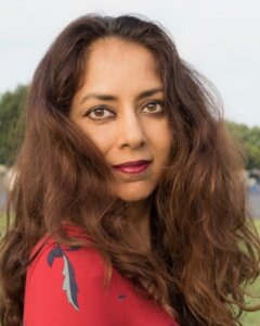 Portrait of Ms. Shilpa Agarwal, an HUA faculty member, with long wavy brown hair wearing a red dress